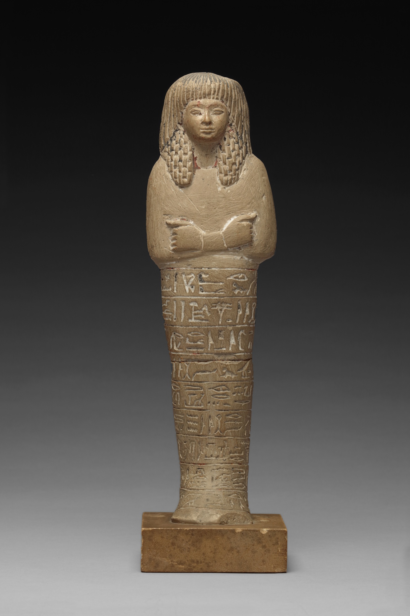 Lord of the North Wind, Governor of the Southern Oasis, holding a seed-sack over his back and wearing a double wig of straight and echeloned curls, the nine lines of engraved inscription naming the owner, his titles, and reciting Spell VI of the Book of the Dead on his behalf, the implements formerly painted. — An Egyptian Polychrome Limestone Ushabti of Neb-mehyt (Nebmehite), 19th Dynasty, 1292-1190 B.C.