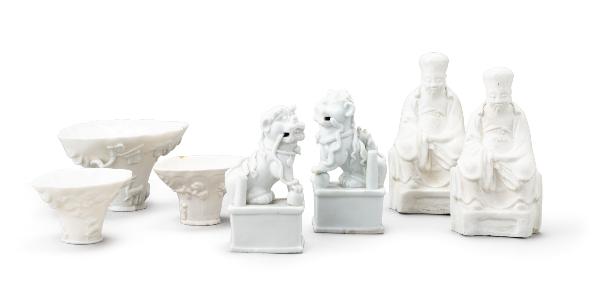 Two blanc de Chine figures of lion dogs and three blanc de Chine libation cups — 清十七至十八世紀 德化白瓷佛獅、盃及 白瓷人物坐像 一組七件