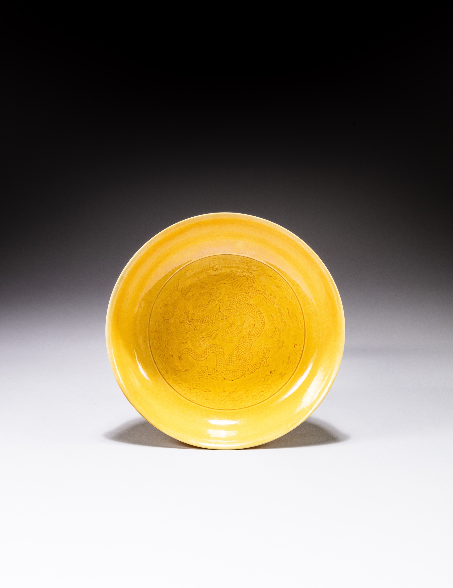 A yellow-glazed incised 'dragon' dish — 清康熙 黃釉暗刻雲龍紋盤《大清康熙年製》款